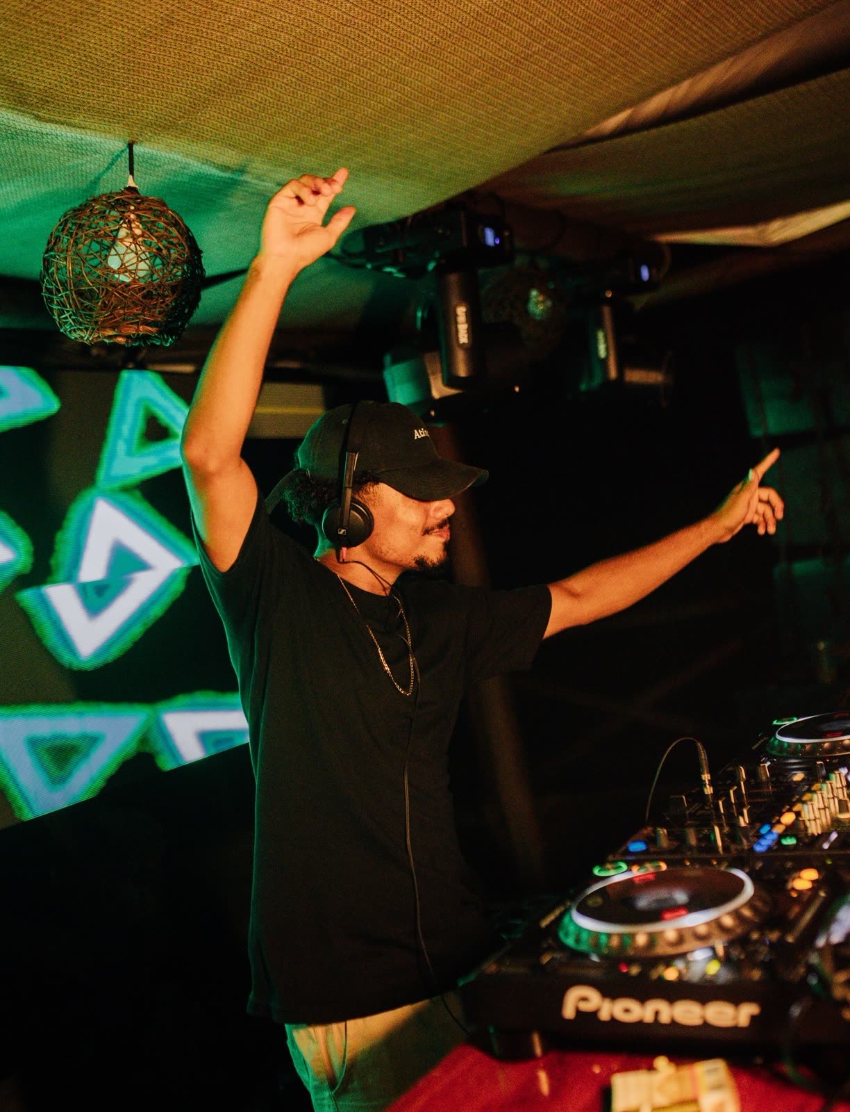 Alesso na cabine com os braços para o alto sob luz verde